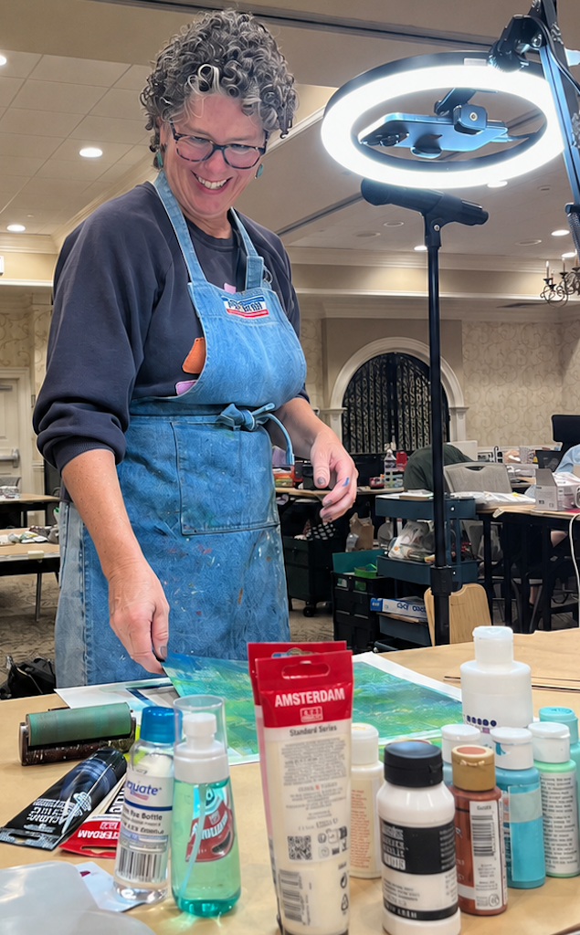 Francine Dunigan in a paint splattered apron, working on a gel print at a workshop table